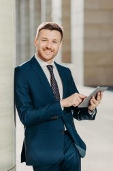 vertical-shot-of-business-person-uses-digital-tablet-for-online-communication-and-work-uses-free-internet-at-office-has-positive-expression-dressed-in-formal-black-suit-people-and-occupation-free-photo